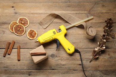 Photo of Hot glue gun and handicraft materials on wooden background, flat lay