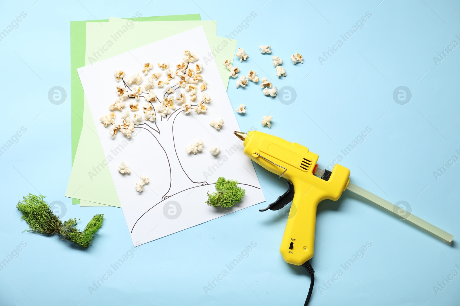 Photo of Hot glue gun and handicraft materials on light blue background, flat lay