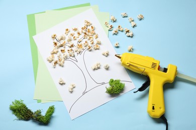 Photo of Hot glue gun and handicraft materials on light blue background, flat lay