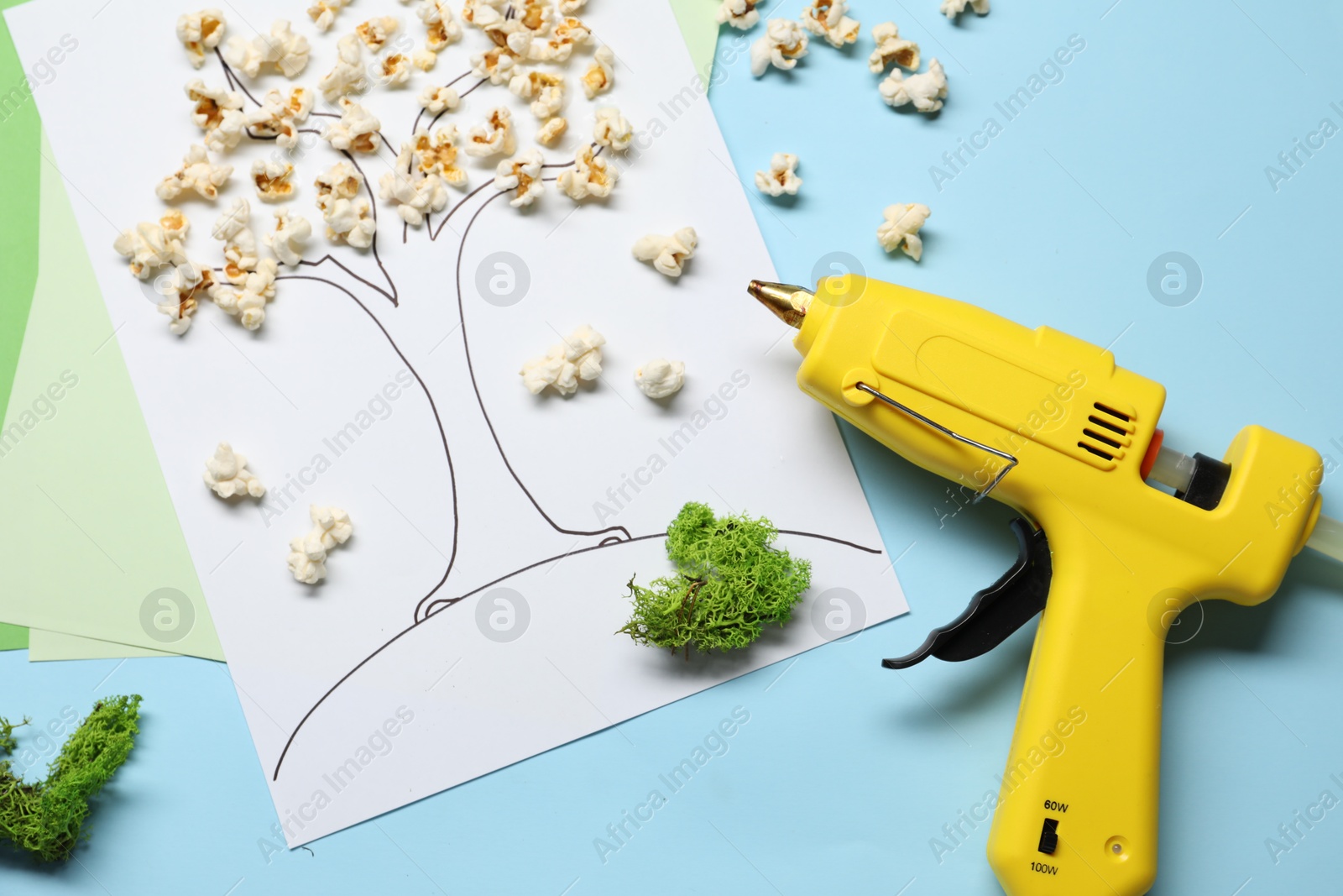 Photo of Hot glue gun and handicraft materials on light blue background, flat lay