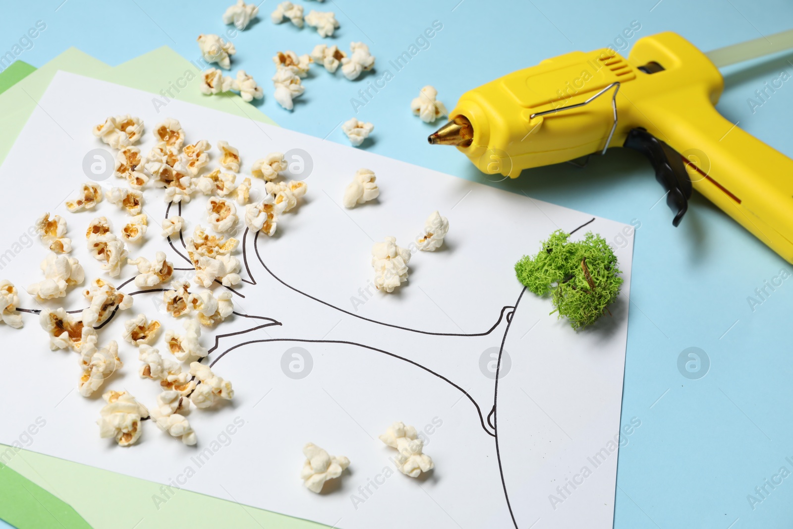 Photo of Hot glue gun and handicraft materials on light blue background, closeup