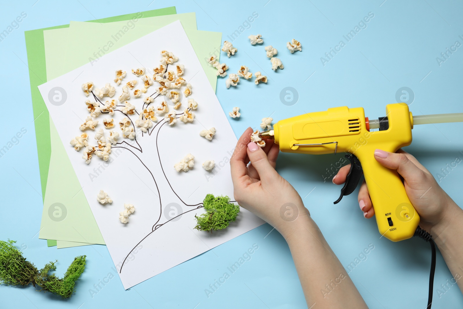 Photo of Woman with hot glue gun making craft on light blue background, top view