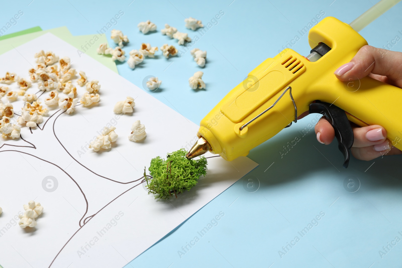 Photo of Woman with hot glue gun making craft on light blue background, closeup