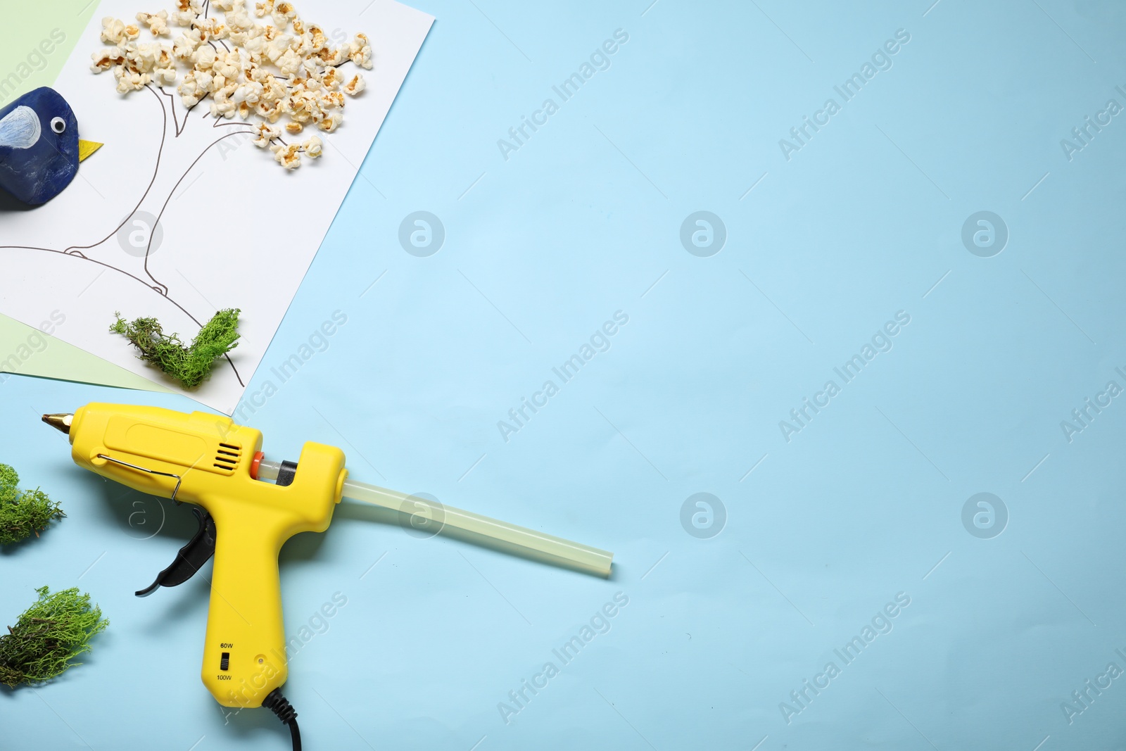 Photo of Hot glue gun and handicraft materials on light blue background, flat lay. Space for text