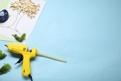 Photo of Hot glue gun and handicraft materials on light blue background, flat lay. Space for text