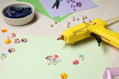 Photo of Hot glue gun and handicraft materials on wooden background, closeup