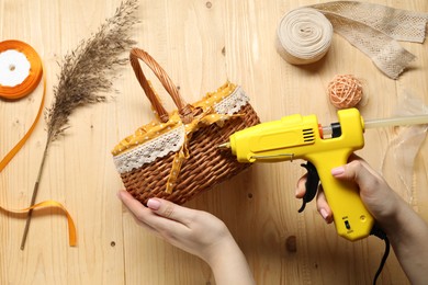 Photo of Woman with hot glue gun making craft at wooden table, top view