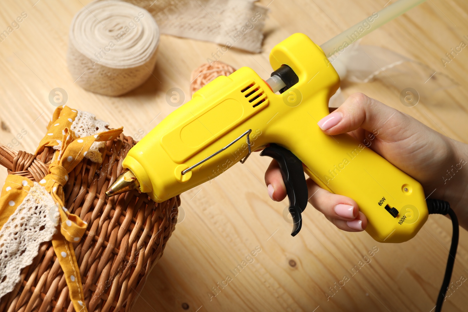 Photo of Woman with hot glue gun making craft at wooden table, closeup