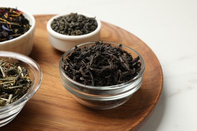 Photo of Different dry tea leaves in bowls on white marble table, closeup