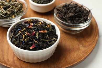 Photo of Different dry tea leaves in bowls on white table, closeup