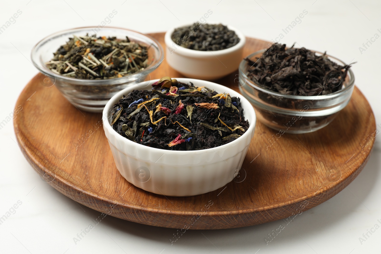 Photo of Different dry tea leaves in bowls on white table, closeup