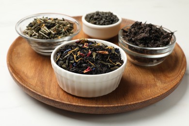 Photo of Different dry tea leaves in bowls on white table, closeup