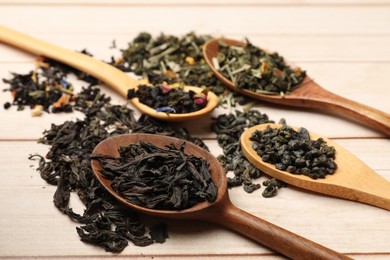 Photo of Different dry tea leaves in spoons on wooden table, closeup