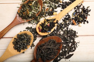 Photo of Different dry tea leaves in spoons on wooden table, flat lay