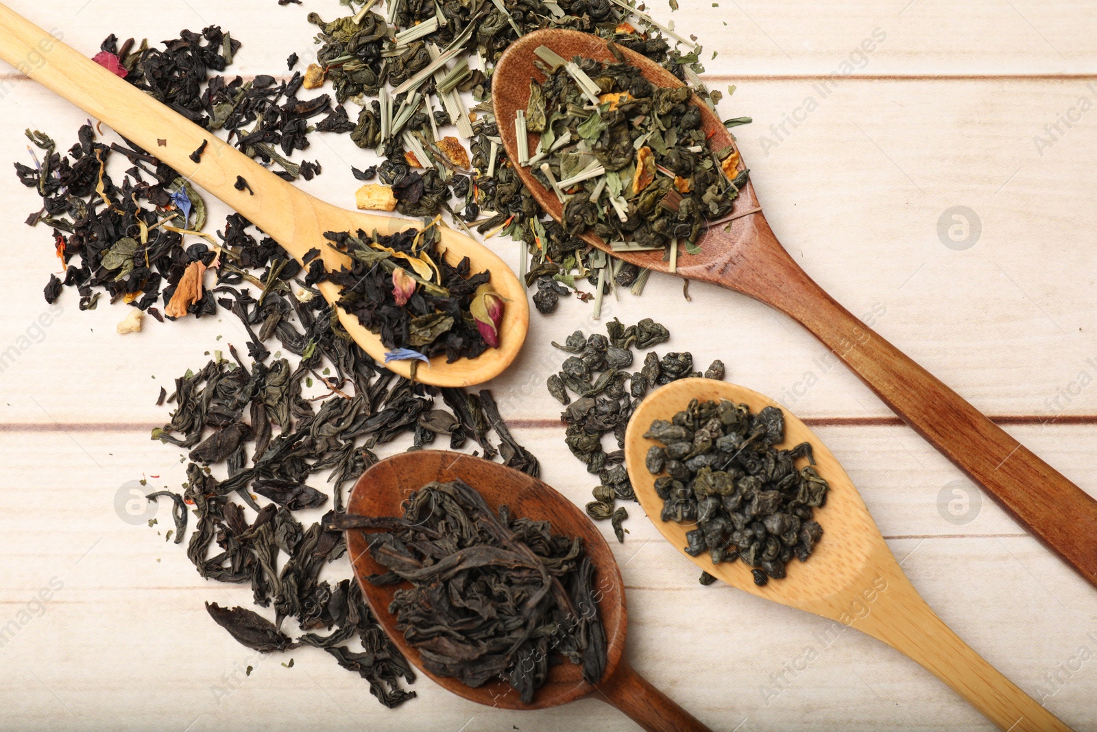 Photo of Different dry tea leaves in spoons on wooden table, flat lay