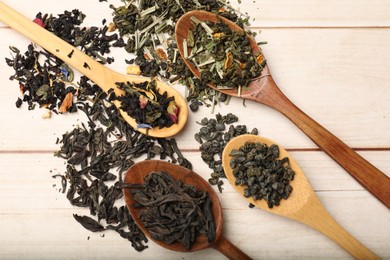 Photo of Different dry tea leaves in spoons on wooden table, flat lay