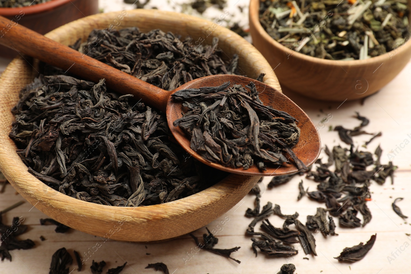 Photo of Different dry tea leaves in bowls and spoon on wooden table, closeup