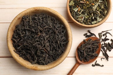 Photo of Different dry tea leaves in bowls and spoon on wooden table, flat lay