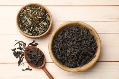 Photo of Different dry tea leaves in bowls and spoon on wooden table, flat lay