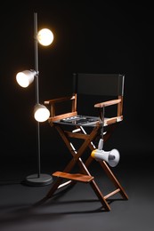 Photo of Director's chair with clapperboard, megaphone and lighting equipment on black background