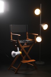 Photo of Director's chair with clapperboard, megaphone and lighting equipment on black background