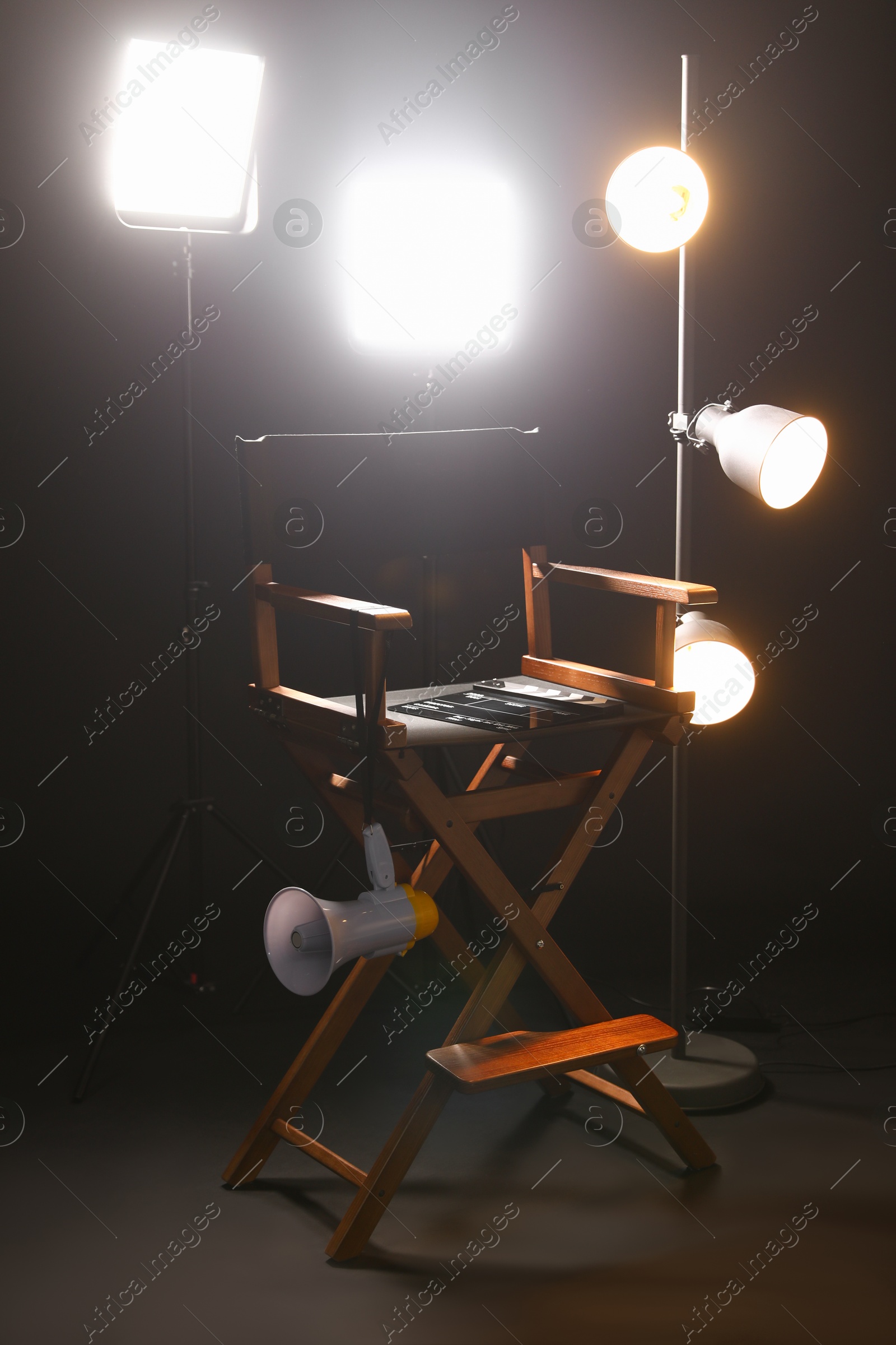 Photo of Director's chair with clapperboard, megaphone and lighting equipment on black background