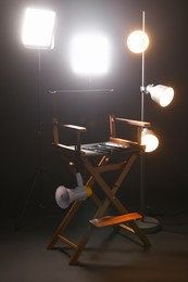 Photo of Director's chair with clapperboard, megaphone and lighting equipment on black background