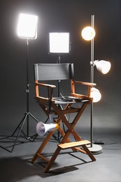 Photo of Director's chair with clapperboard, megaphone and lighting equipment on black background