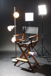 Photo of Director's chair with clapperboard, megaphone and lighting equipment on black background