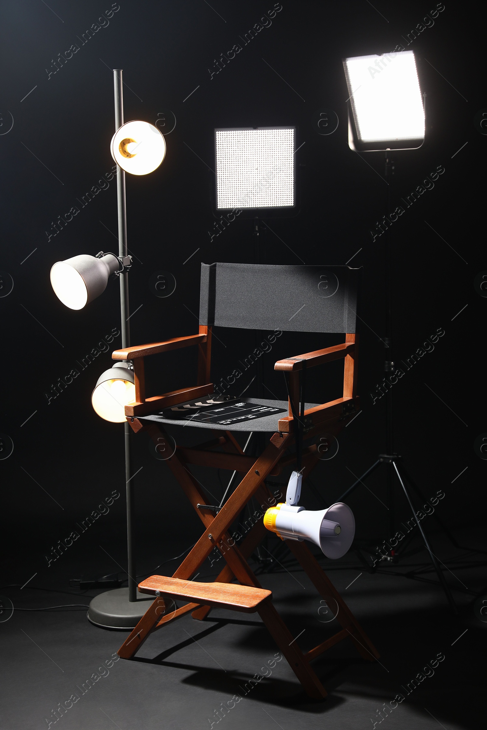 Photo of Director's chair with clapperboard, megaphone and lighting equipment on black background