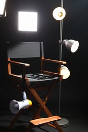 Photo of Director's chair with clapperboard, megaphone and lighting equipment on black background