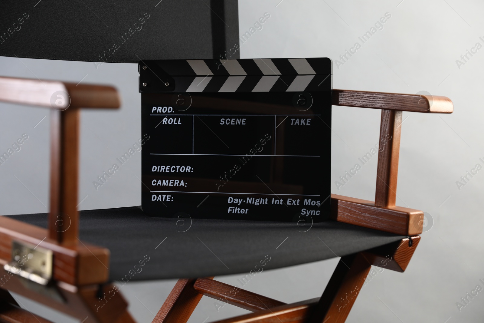 Photo of Director's chair with clapperboard on light grey background, closeup