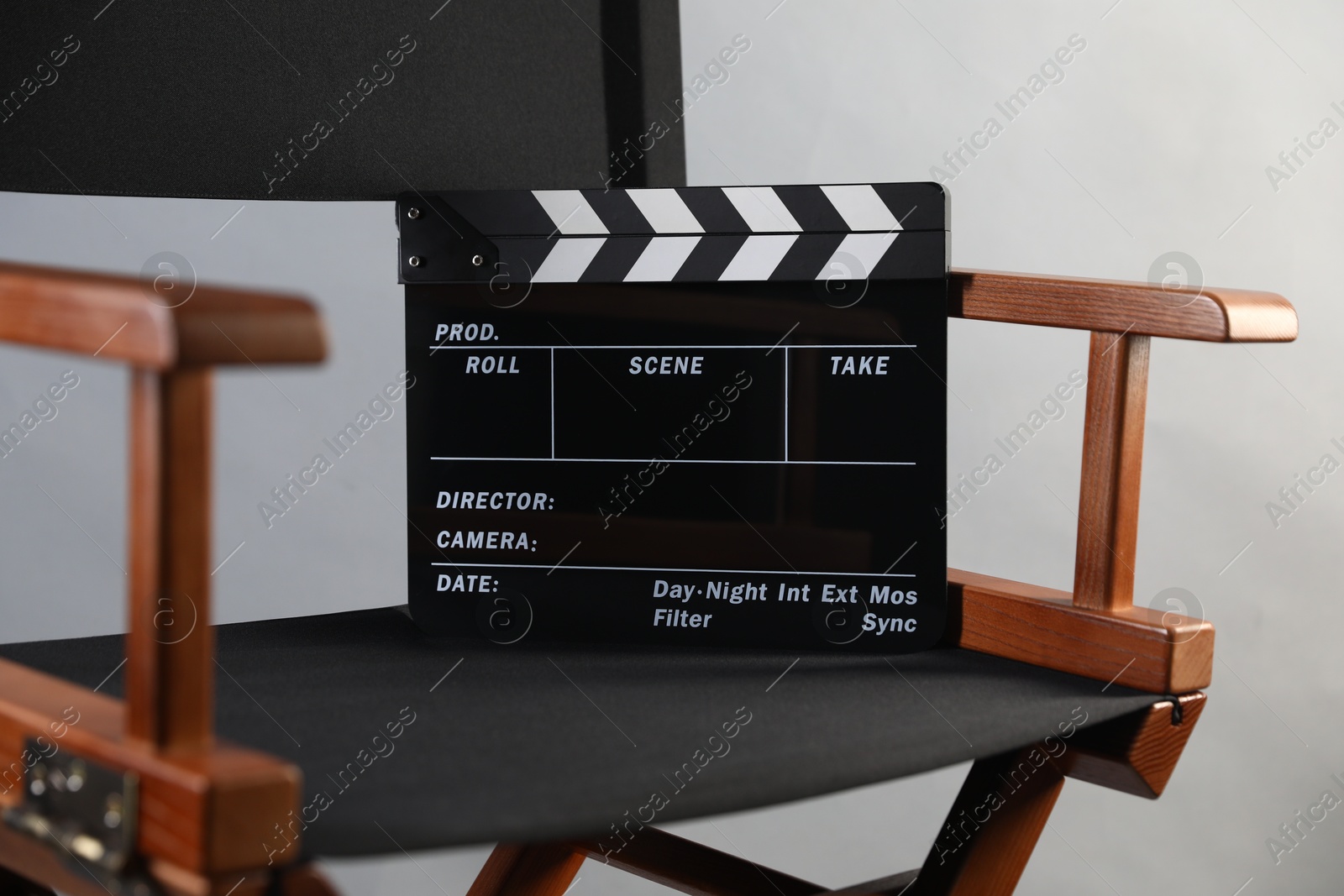 Photo of Director's chair with clapperboard on light grey background, closeup