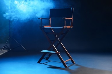 Photo of One empty director's chair on dark blue background with smoke