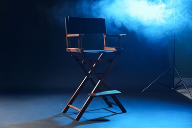 Photo of One empty director's chair on dark blue background with smoke