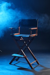 Photo of One empty director's chair on dark blue background with smoke