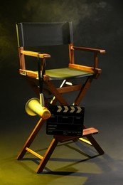 Photo of Director's chair with clapperboard and megaphone on dark background with smoke