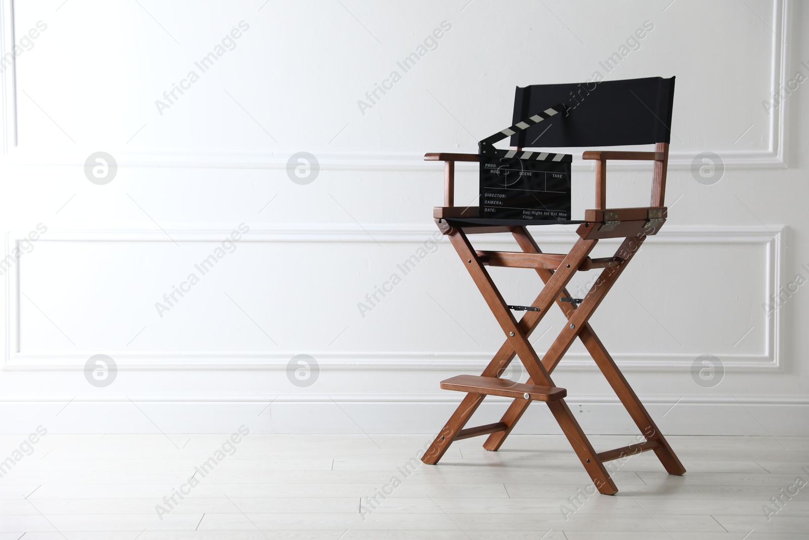 Photo of Director's chair with clapperboard near white wall indoors, space for text