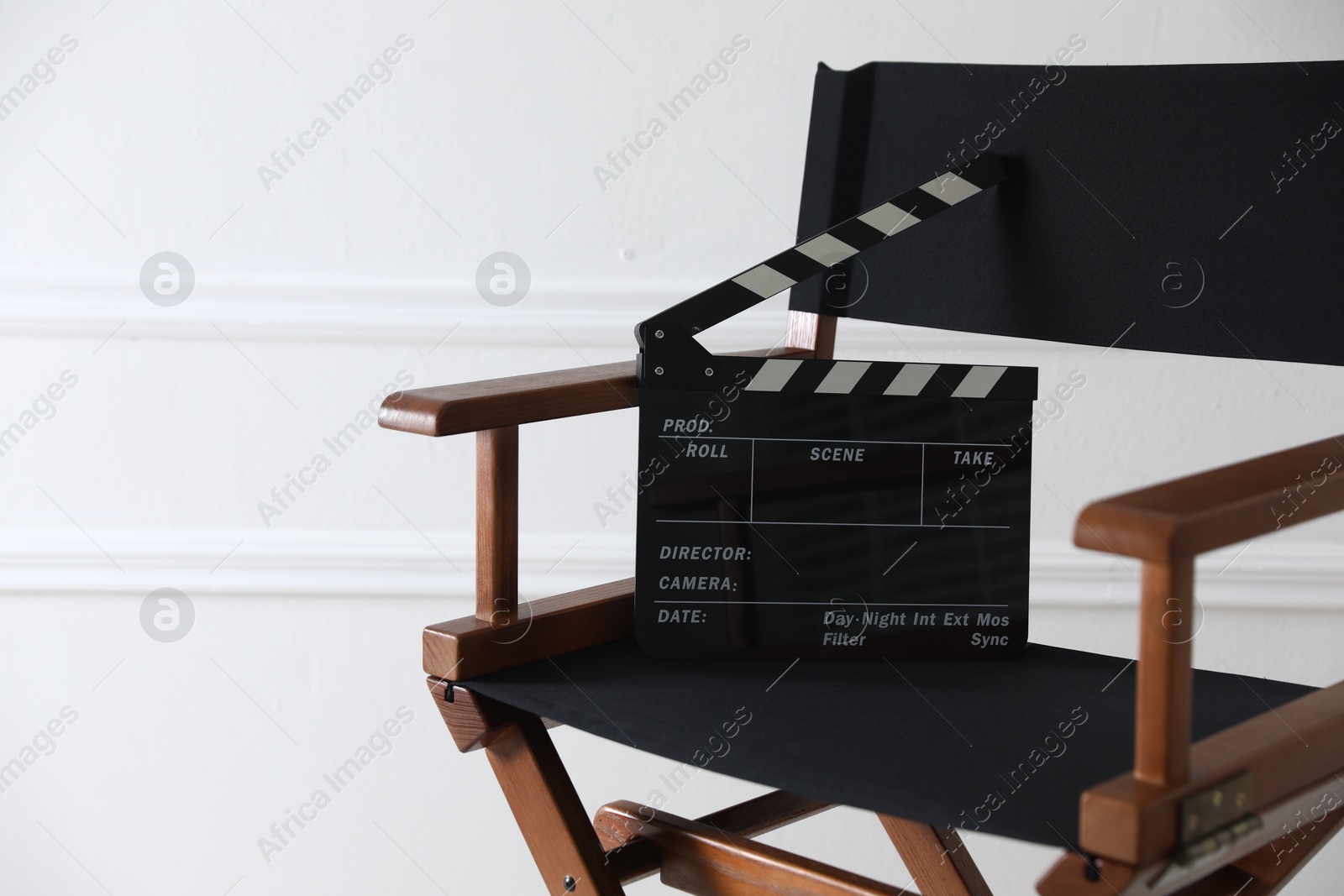 Photo of Director's chair with clapperboard near white wall indoors, closeup. Space for text