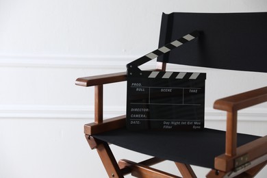 Photo of Director's chair with clapperboard near white wall indoors, closeup. Space for text