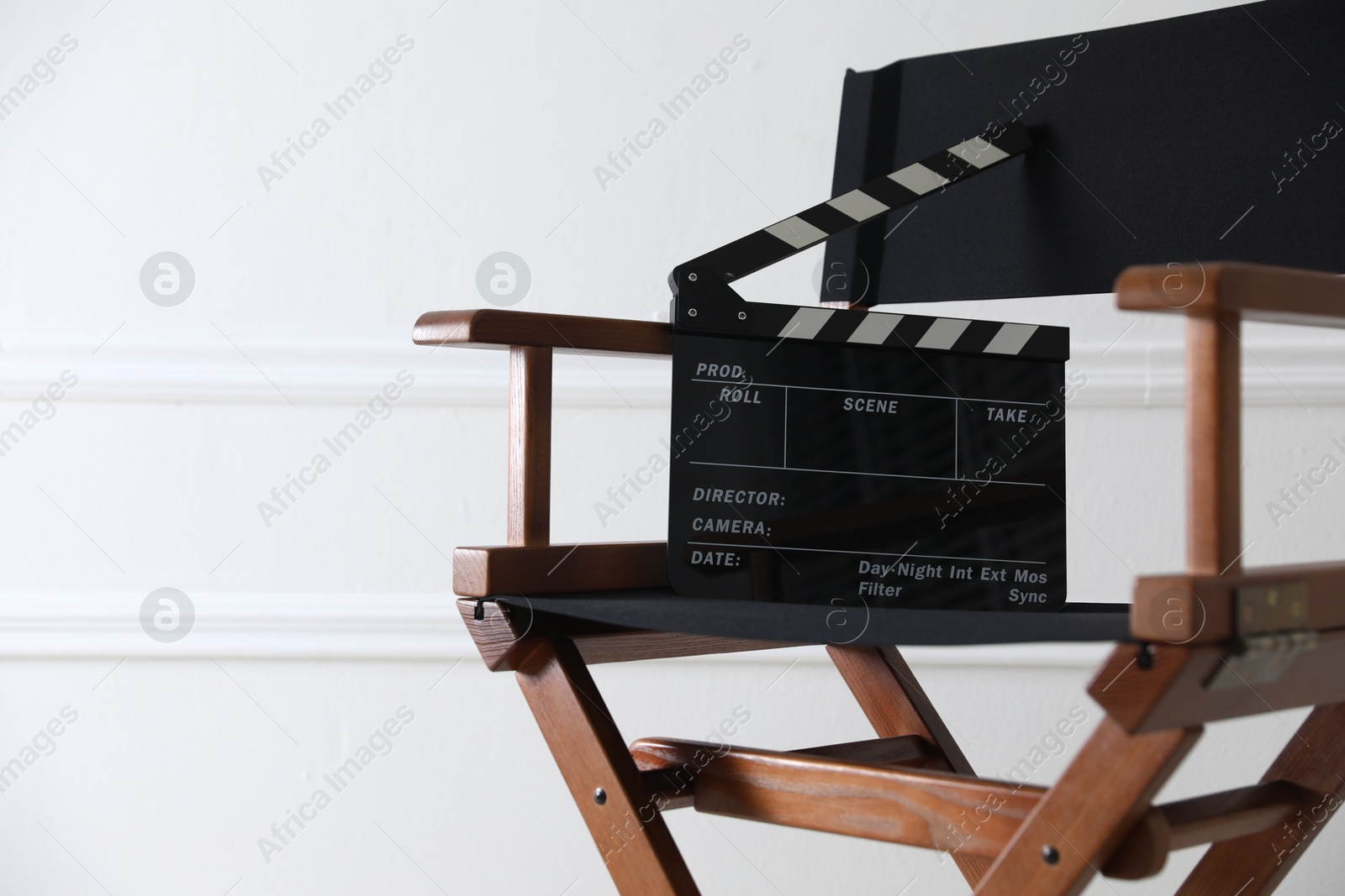 Photo of Director's chair with clapperboard near white wall indoors, closeup. Space for text