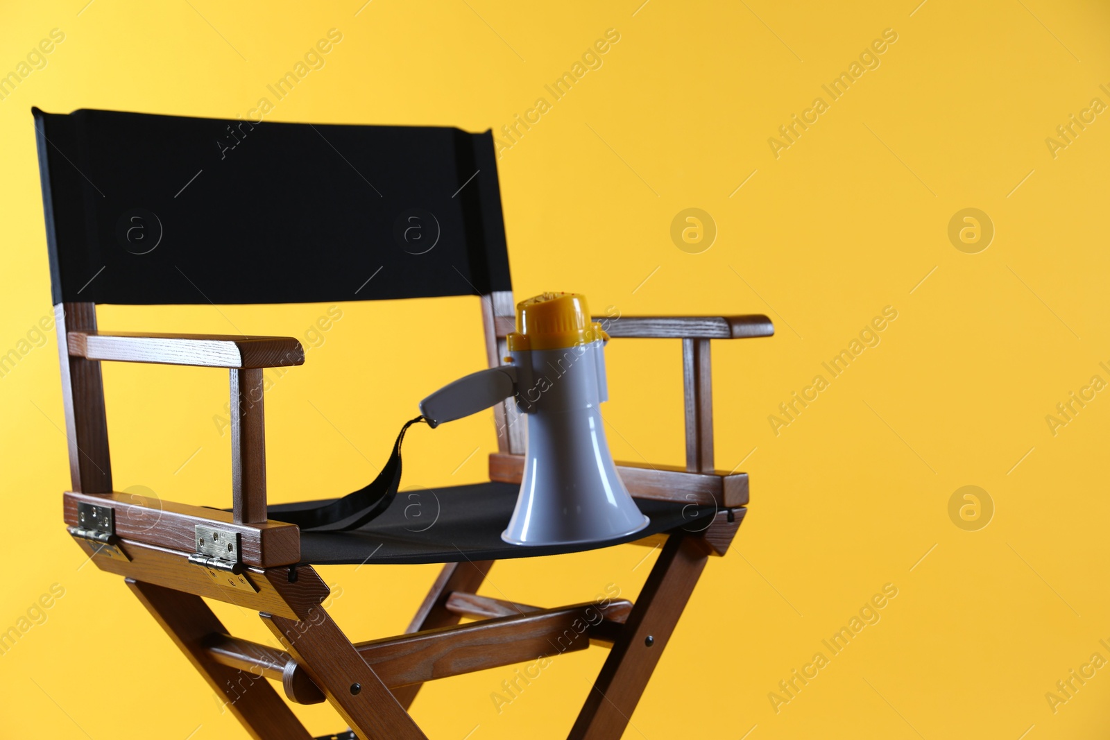 Photo of Director's chair with megaphone on yellow background, closeup. Space for text