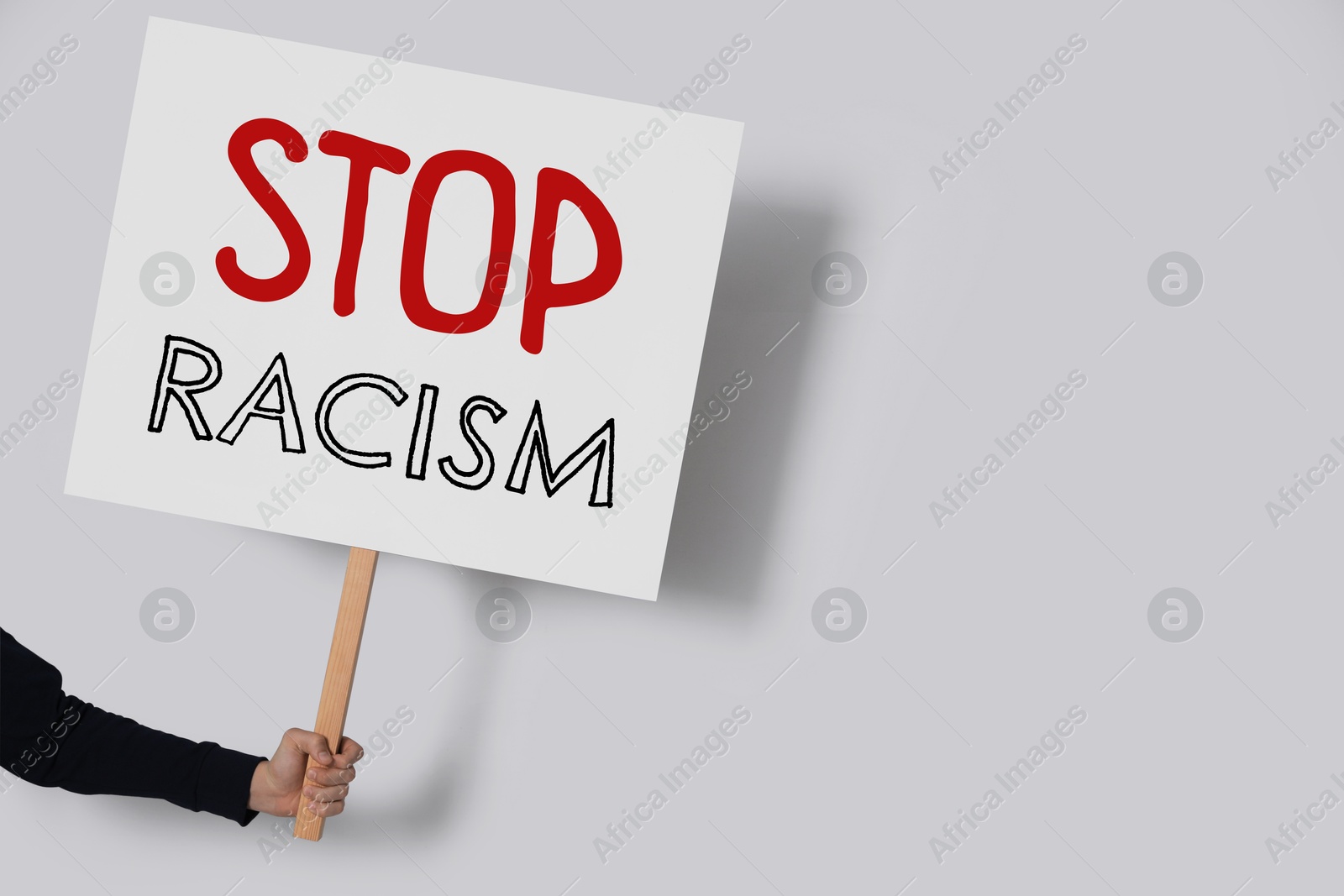 Image of Woman holding sign with text Stop Racism on light grey background, closeup. Space for text