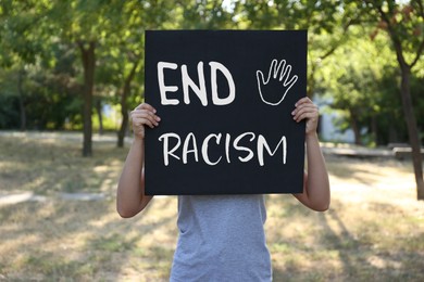 Image of Woman holding black poster with text End Racism outdoors