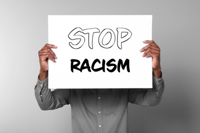 Image of Man holding paper with text Stop Racism on grey background, closeup