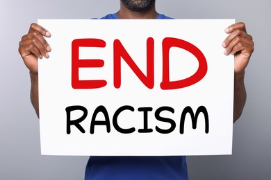 Man holding paper with text End Racism on grey background, closeup