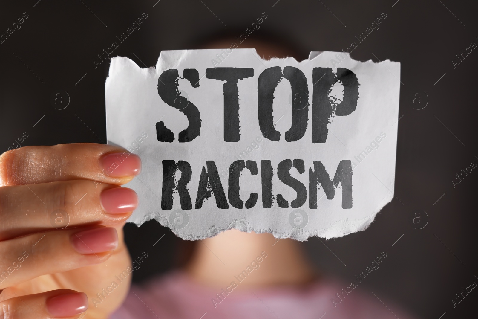 Image of Woman holding piece of paper with text Stop Racism on dark background, closeup