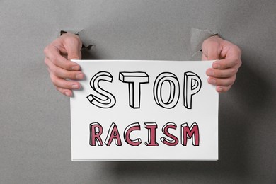 Image of Man holding paper with text Stop Racism through holes in grey paper, closeup