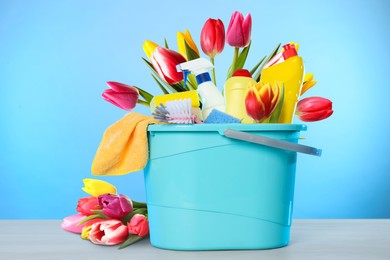 Image of Spring cleaning. Bucket with detergents, supplies and tulips on light blue background