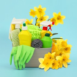 Image of Spring cleaning. Basket with detergents, supplies and daffodils on light blue background